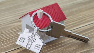 keychain with house symbol and keys on wooden background