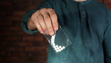 Male dealer holding drugs in plastic bag near brick wall