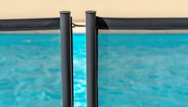 Swimming Pool through a mandatory safety net on the edges of a private psicine|barrier for the safety of children with a pool in the background|Swimming pool alarm on the side of an in ground pool with a child in the water|Children are drowning in danger.
