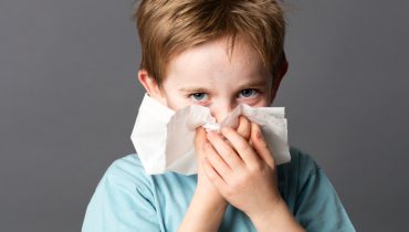 beautiful boy using tissue to clean his nose after cold